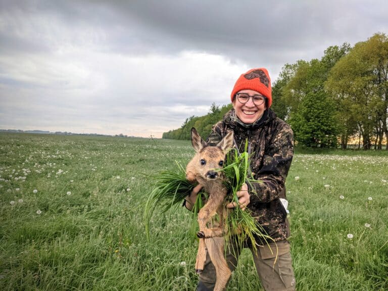 Jägerin bei der Rehkitzrettung. Eine Frau hält ein Rehkitz mit Handschuhen und Gras in die Höhe um es zu retten.