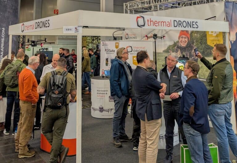 Bild eines Messestandes von thermal DRONES in einer großen Halle. Mehrere Personen stehen davor und unterhalten sich mit Mitarbeitern von thermal DRONES.